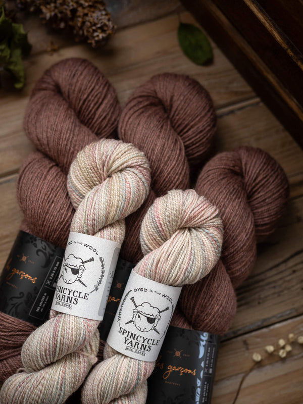 Spincycle Yarns and Les Garçons yarn skeins on a wooden surface with visible labels