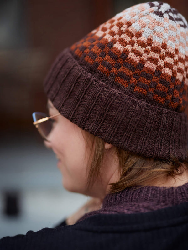 Person wearing a patterned knit hat and glasses with a blurred background
