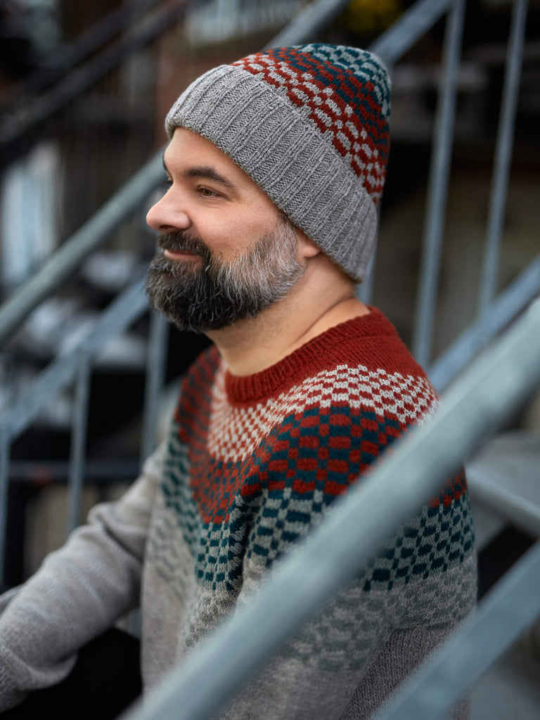 Man wearing a patterned knit hat and sweater sitting on metal stairs.