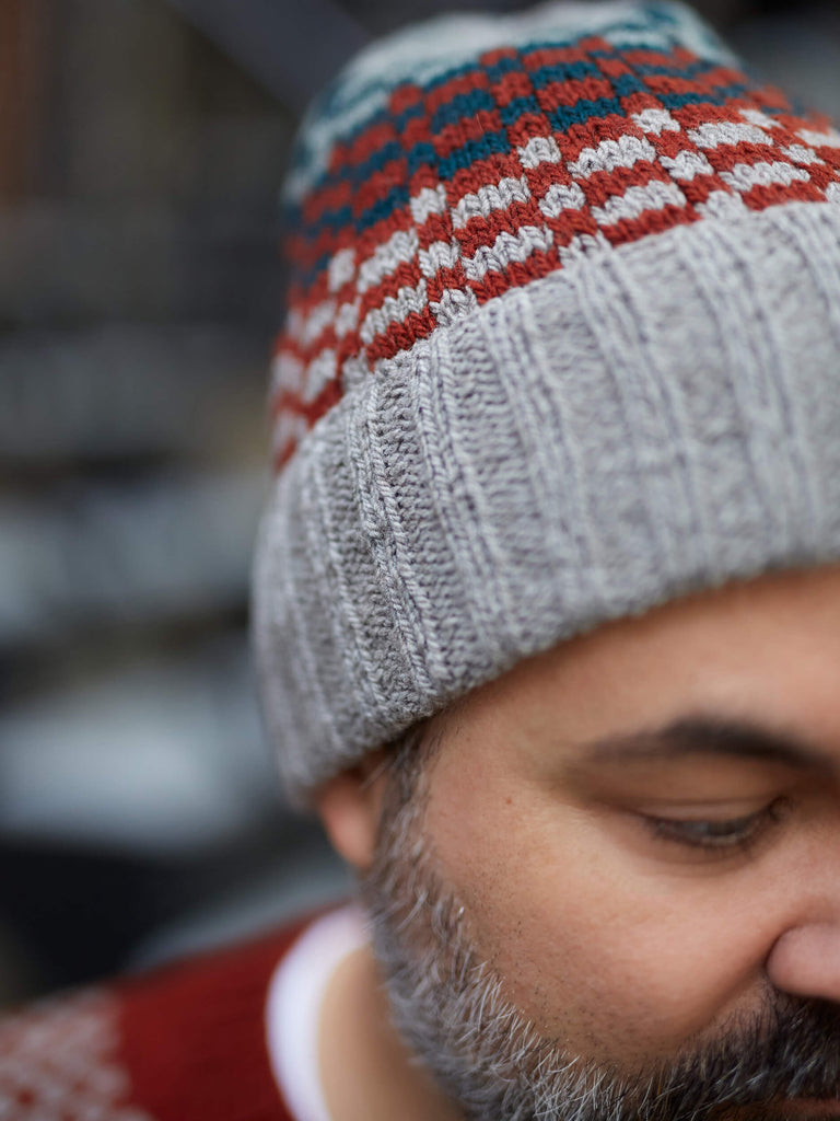 Person wearing a gray knit beanie with red and blue pattern, blurred background